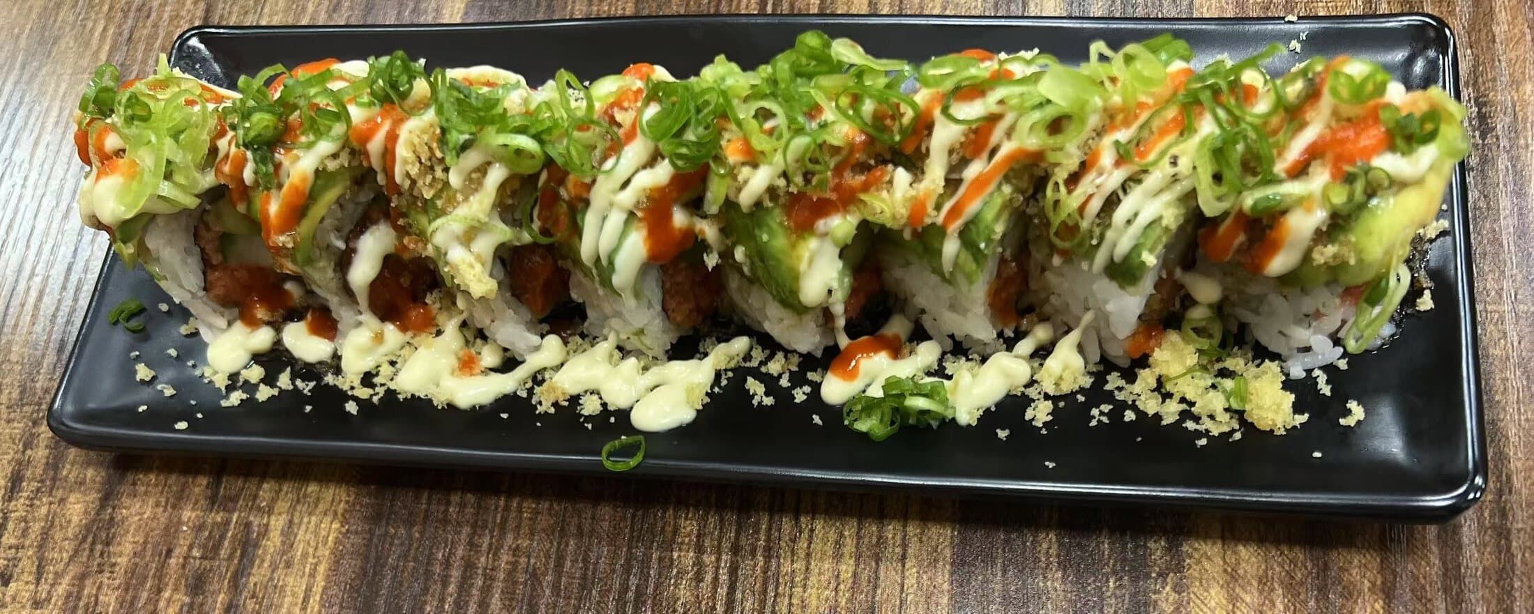 Specialty roll draped in avocado with spicy mayo and scallions